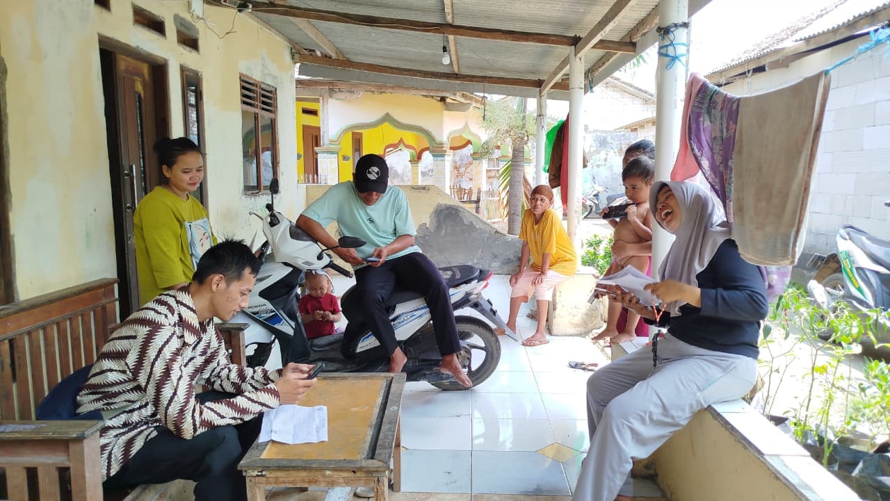 Petugas lapangan mendata warga di teras rumah sambil warga lain menunggu giliran dengan formulir di tangan.