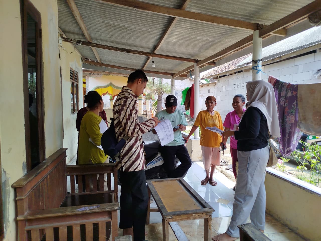 Tim lapangan membagikan dan memeriksa formulir pendaftaran bersama warga di teras rumah.