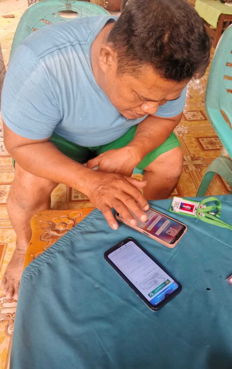 Seorang warga mengaktifkan aplikasi Mobile JKN di ponselnya dibantu tim lapangan.