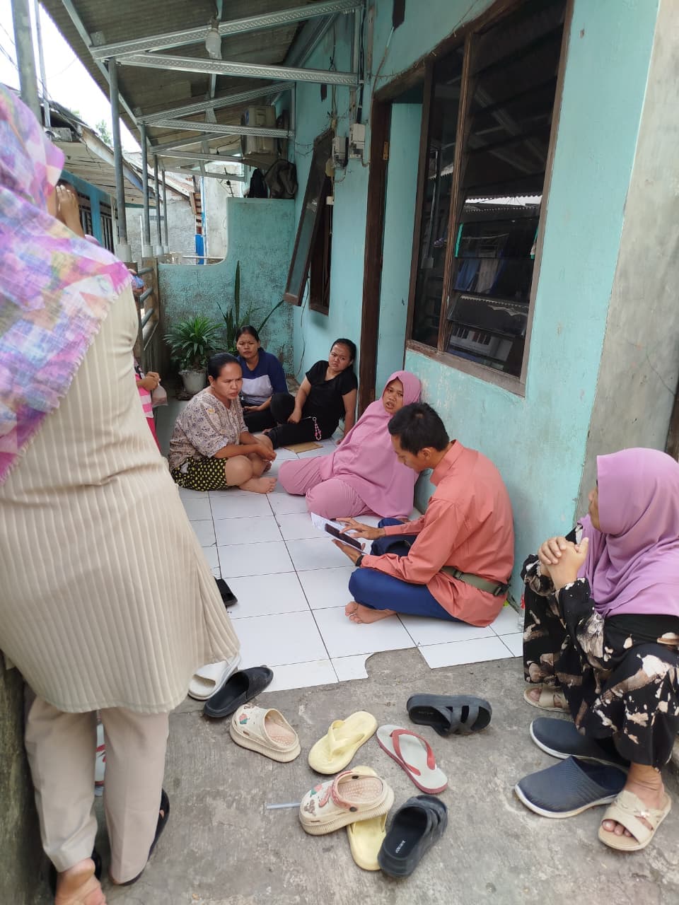 Sekelompok ibu duduk melingkar mendengarkan penjelasan tim lapangan di teras rumah.