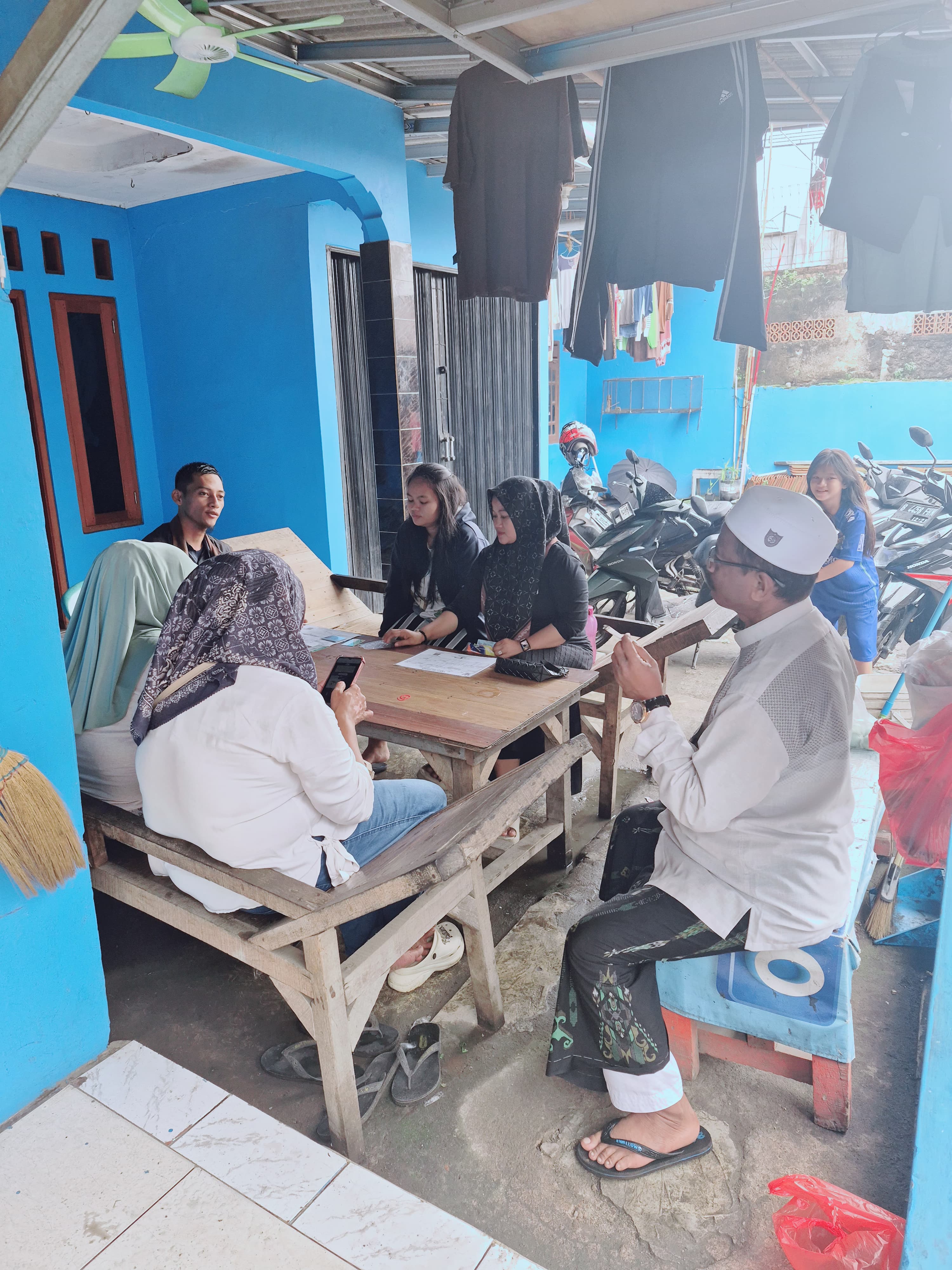 Tim lapangan menjelaskan program kepada warga dan tokoh masyarakat di teras sebuah rumah.
