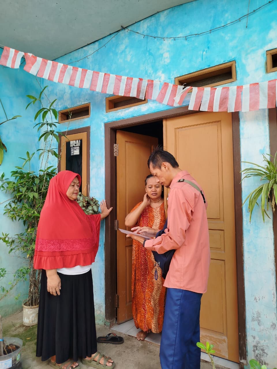 Petugas lapangan menjelaskan isi formulir kepada dua warga di depan pintu rumah.