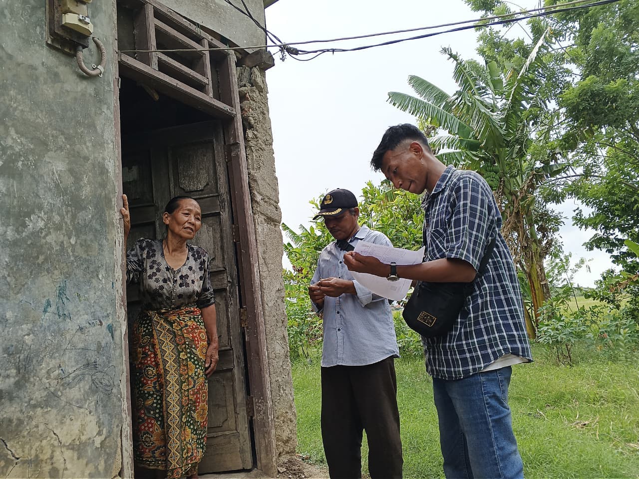 Petugas lapangan bersama perangkat lingkungan mendatangi rumah seorang warga lanjut usia.