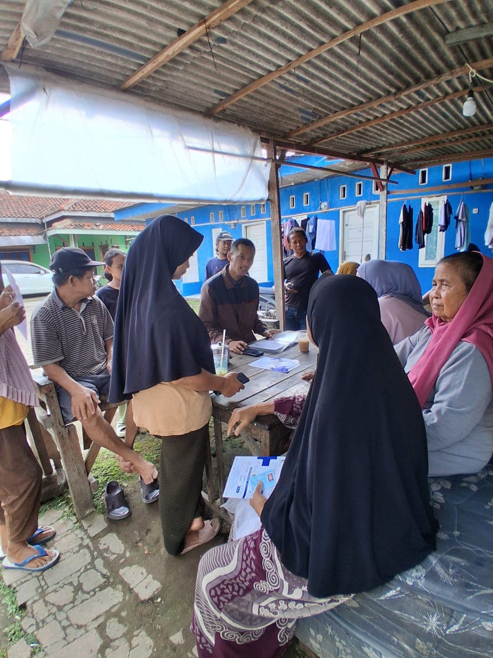 Warga memegang kartu peserta JKN sambil berbincang dengan tim lapangan di bawah tenda.