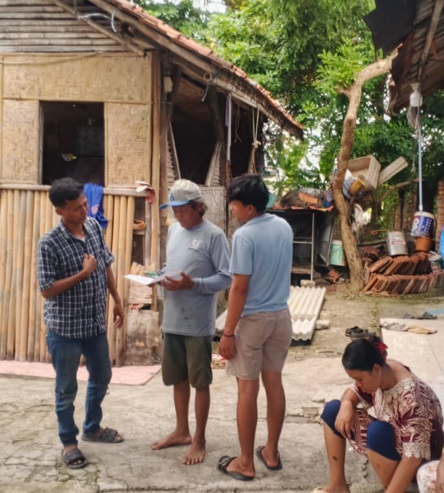 Petugas lapangan berbincang dengan dua warga di halaman rumah sambil membawa berkas.